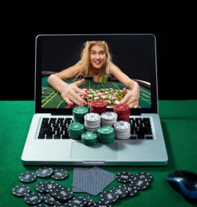 Green table with casino chips, cards on notebook, image of poker player on screen of laptop. Concept for online gambling.